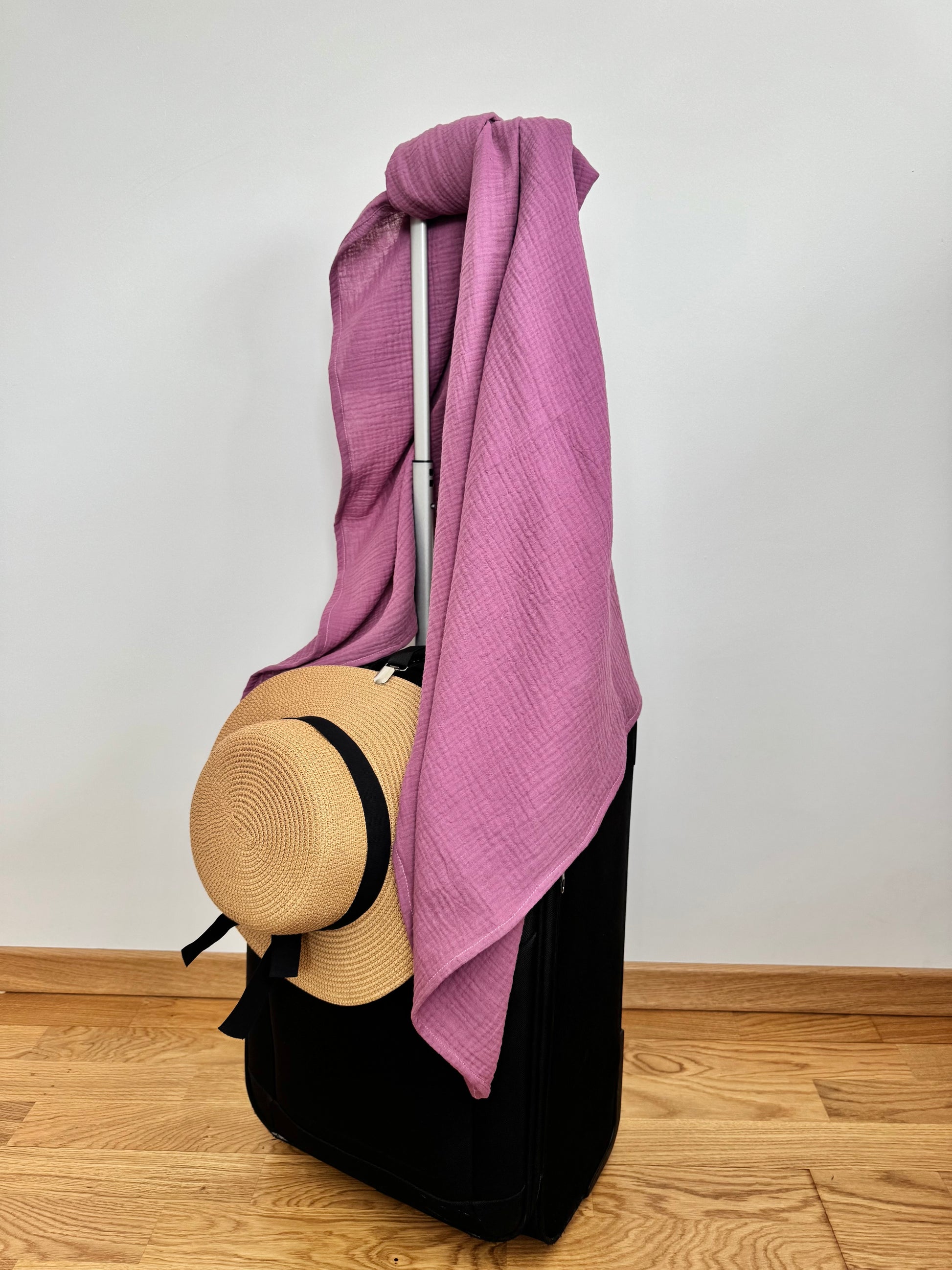 Dusty rose pink scarf wrap blanket draped over a suitcase with a straw hat 